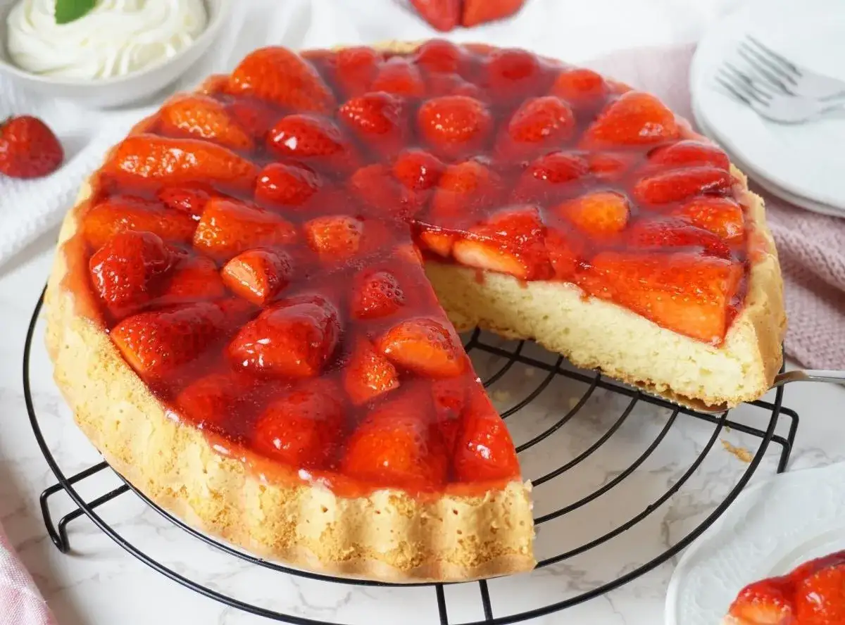 Saftige Erdbeertorte mit Tortenguss auf einem Gitterrost. Ein St&uuml;ck ist bereits herausgeschnitten. Dieses Erdbeertorte Rezept ist ein Klassiker.