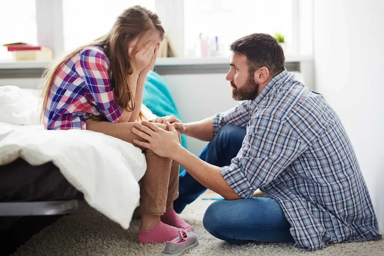 Pappa tröstar dotter som gråter, kanske på grund av separationsångest. Han håller hennes händer mjukt.