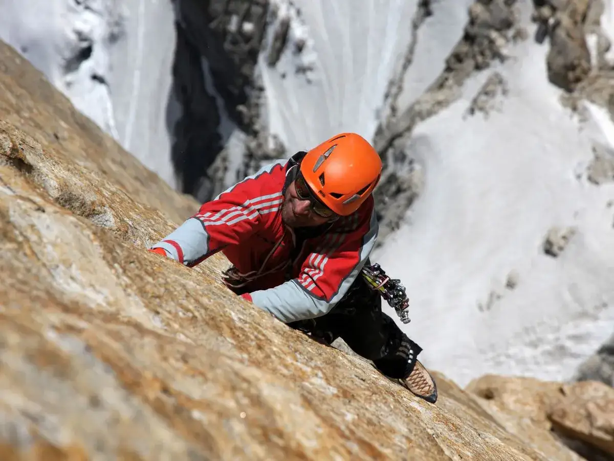Alexander Huber klettert eine steile Felswand empor, im Hintergrund schneebedeckte Berge.