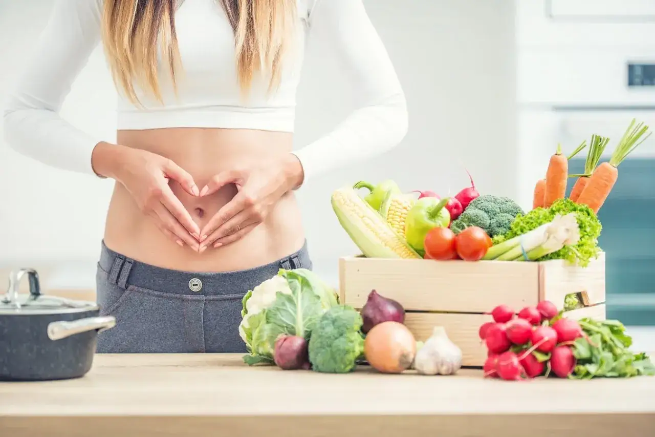 Kobieta z sercem z dłoni na brzuchu, obok skrzynka świeżych warzyw. Idealna dieta dla kobiet.