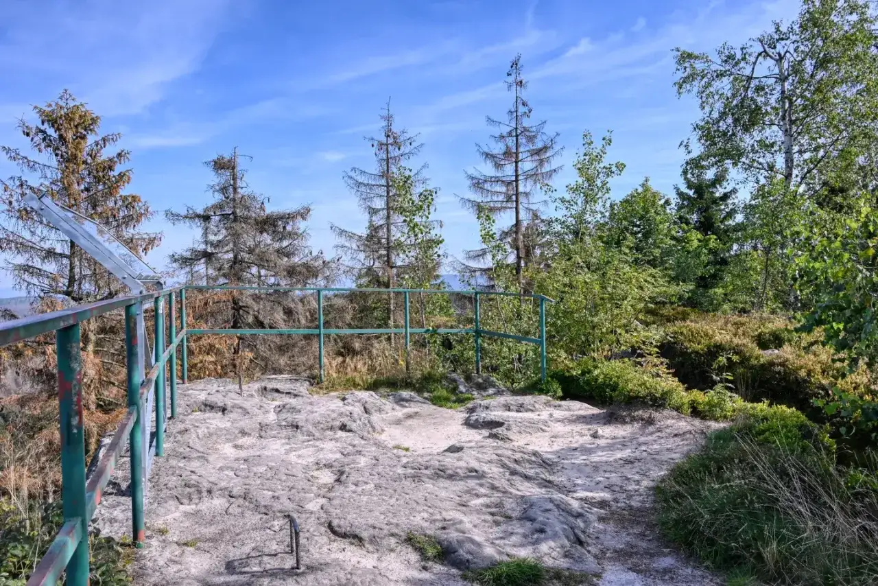 Kamieniste podejście na szczyt z widokiem na las i błękitne niebo. W oddali majaczy **fort Karola**.