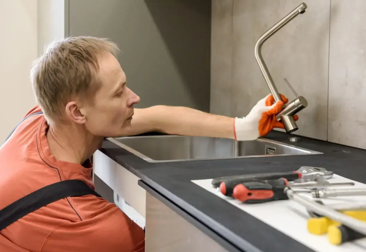Instalator montuje nowy kran, by pozbyć się uciążliwego bulgotania w zlewie. Obok leżą narzędzia.