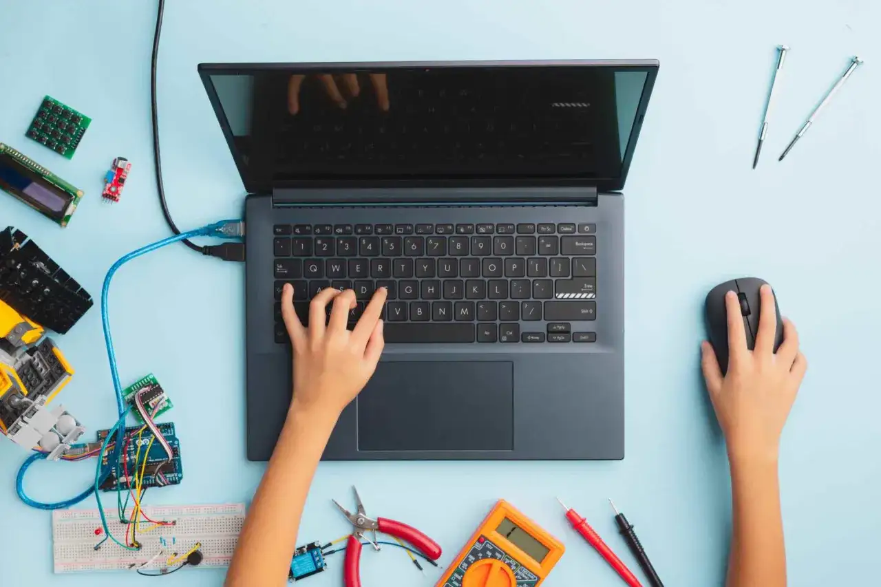 Dziecko uczy się programowania, tworząc projekt z elektroniką. Na stole leży laptop, myszka, płytka stykowa, Arduino i multimetr.