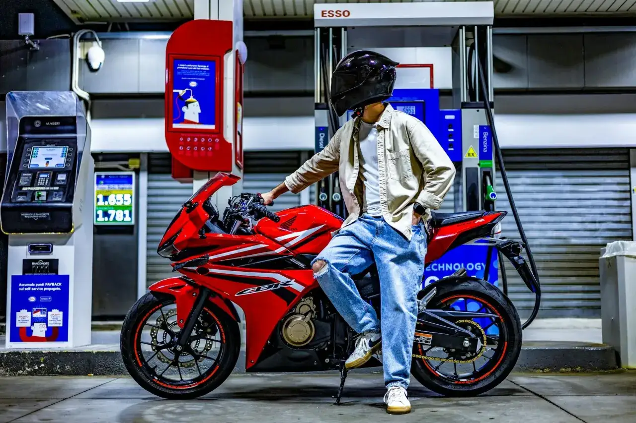 Motocyklista w kasku przy czerwonym motocyklu CBR na stacji paliw. Zastanawia się, ile pali motor 600.