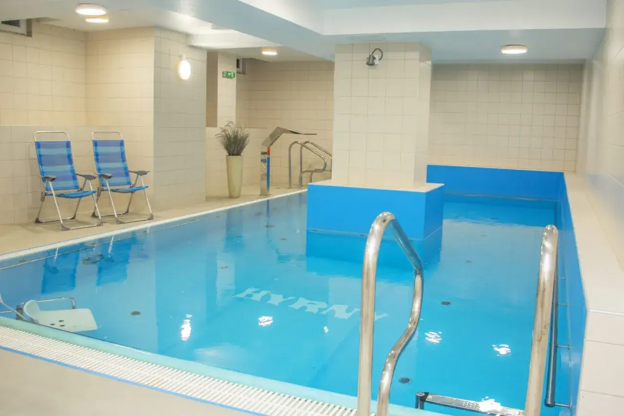 Basen w hotelu Hyrny Zakopane. Sprawdź cennik i zrelaksuj się w wodzie. Dwa leżaki czekają na gości.