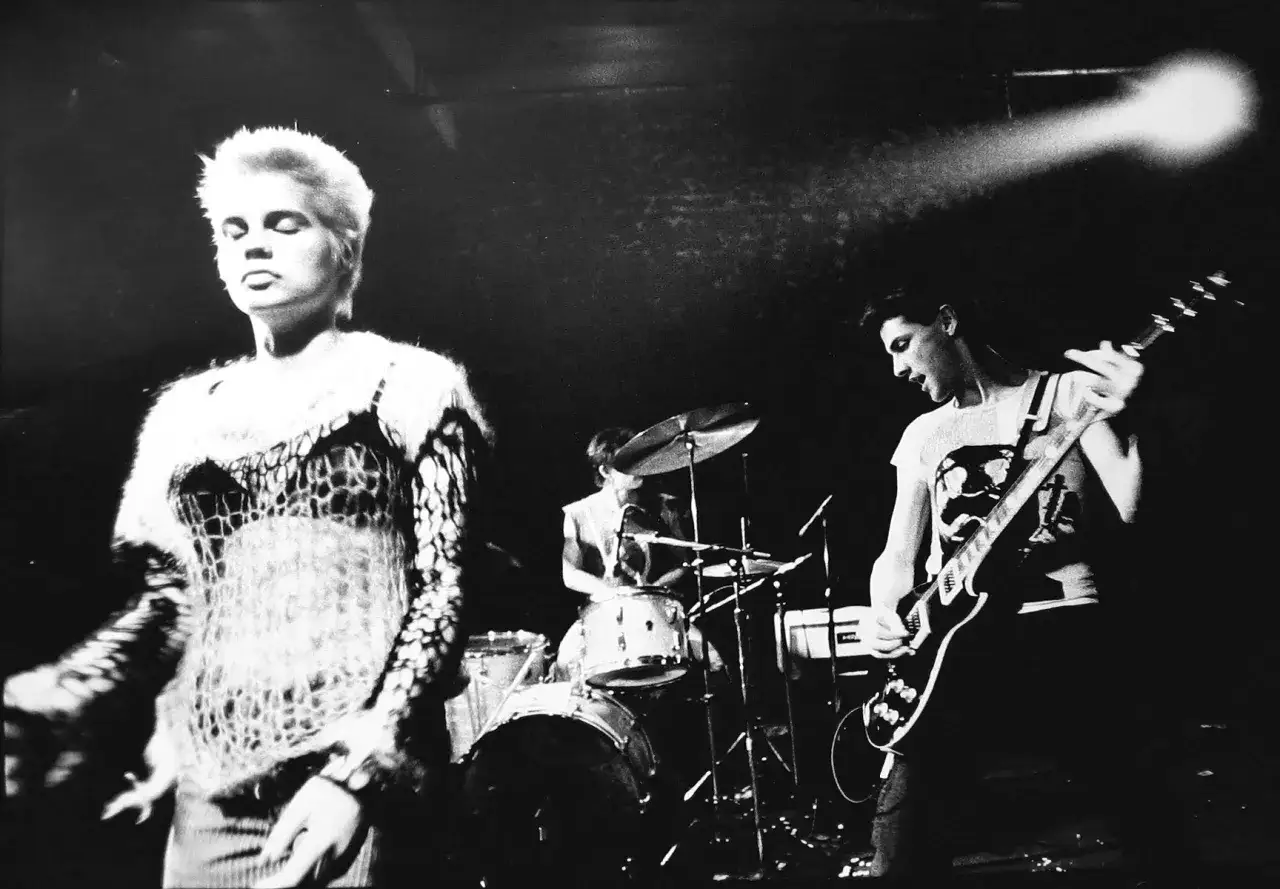 Eine Punkband auf der Bühne. Die Sängerin mit kurzgeschorenen Haaren, der Gitarrist und der Schlagzeuger geben alles.