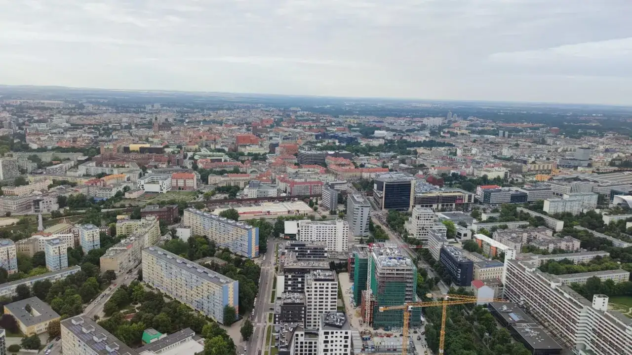 Widok z góry na miasto, widać budynki mieszkalne i biurowe, a w oddali horyzont. Zdjęcia Sky Tower ukazują panoramę.