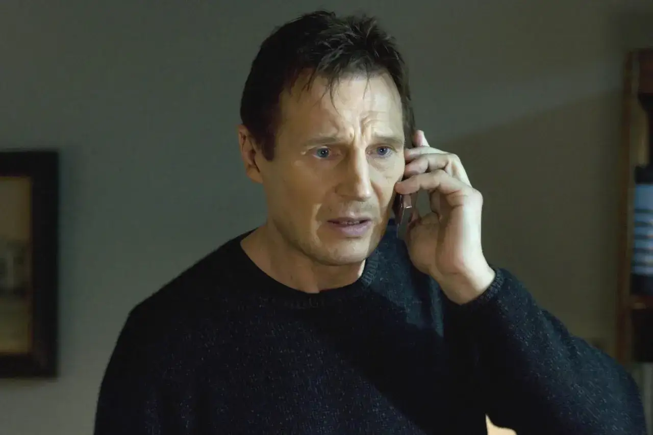 Liam Neeson w jednym z filmów, rozmawia przez telefon, jego twarz wyraża zaniepokojenie.