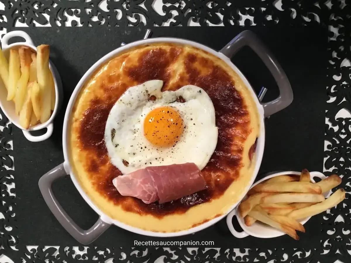Un plat de recette welsh gratin&eacute;, surmont&eacute; d'un &oelig;uf au plat et d'une tranche de jambon, accompagn&eacute; de frites croustillantes.