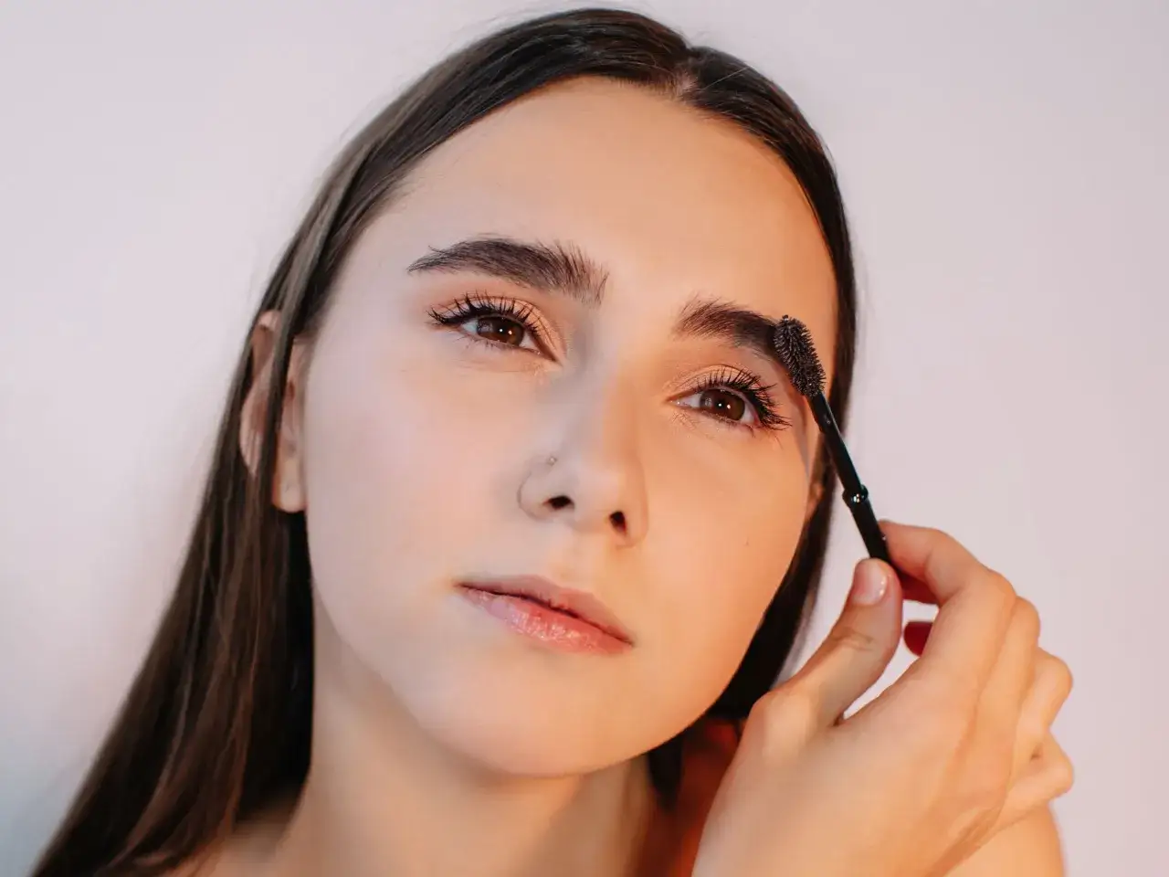 Une jeune femme se maquille, brossant ses sourcils avec une brosse &agrave; mascara.