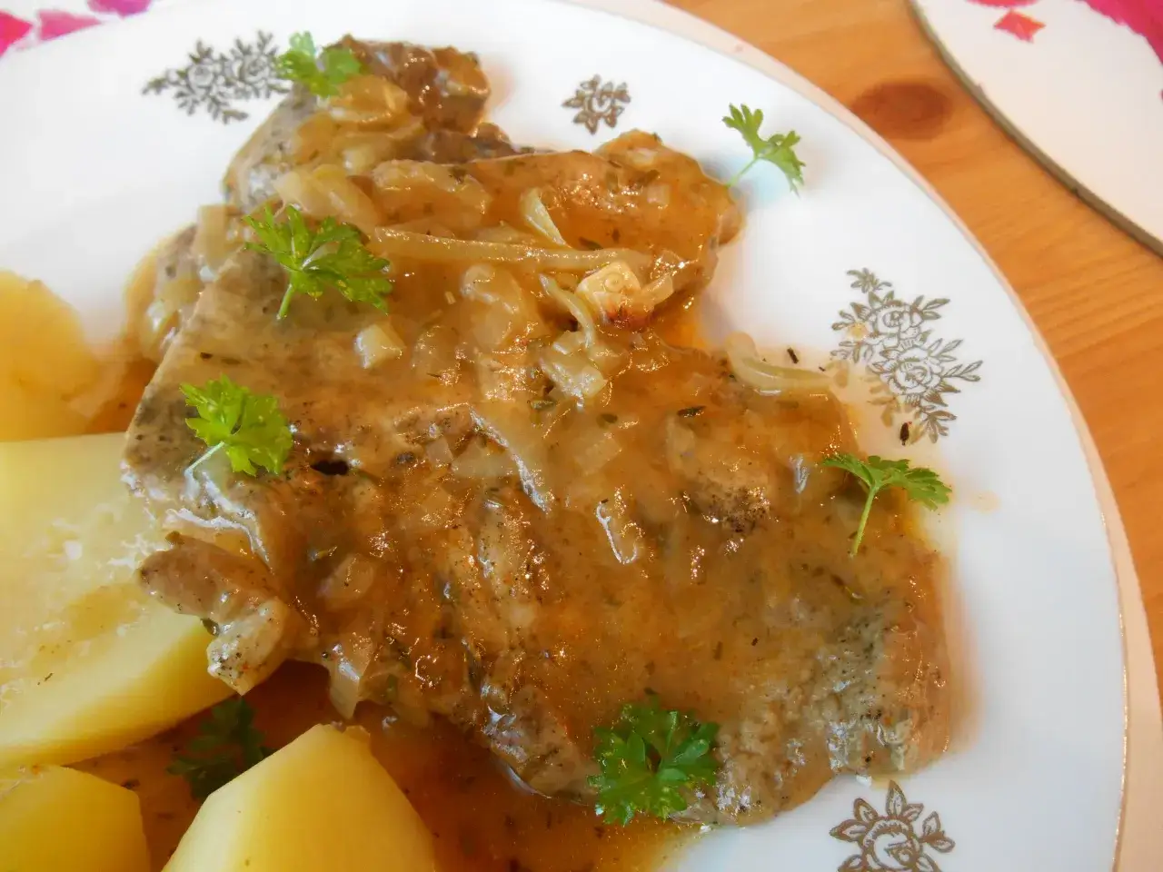 Pyszna karkówka w sosie z cebulką i ziemniakami, udekorowana natką pietruszki. Idealny obiad domowy.