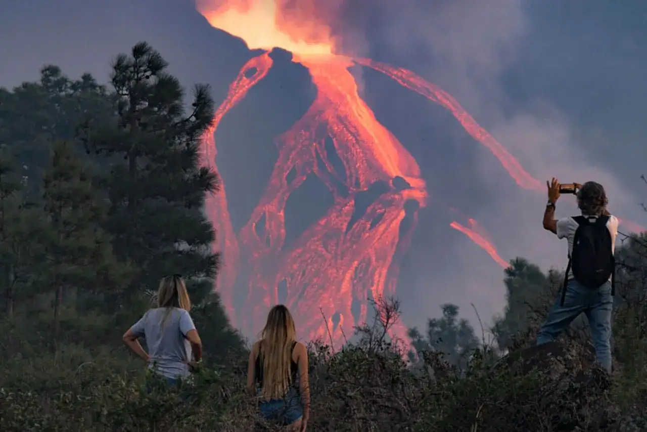 Des spectateurs observent la lave incandescente couler du volcan sur **la Palma**. Un homme prend une photo avec son téléphone.