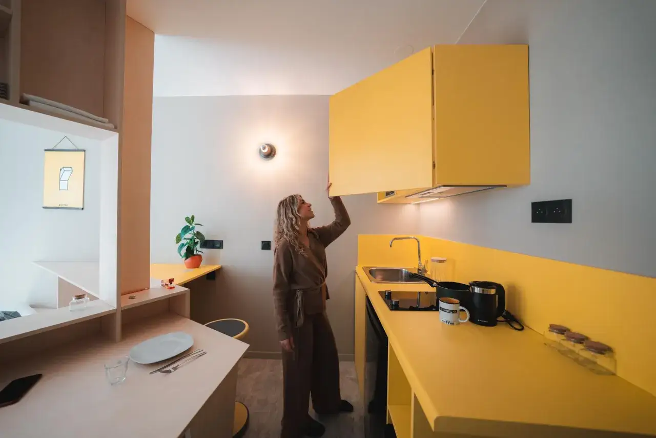 Une femme ouvre un placard jaune vif dans une cuisine moderne, parfaite pour un deco studio etudiant.