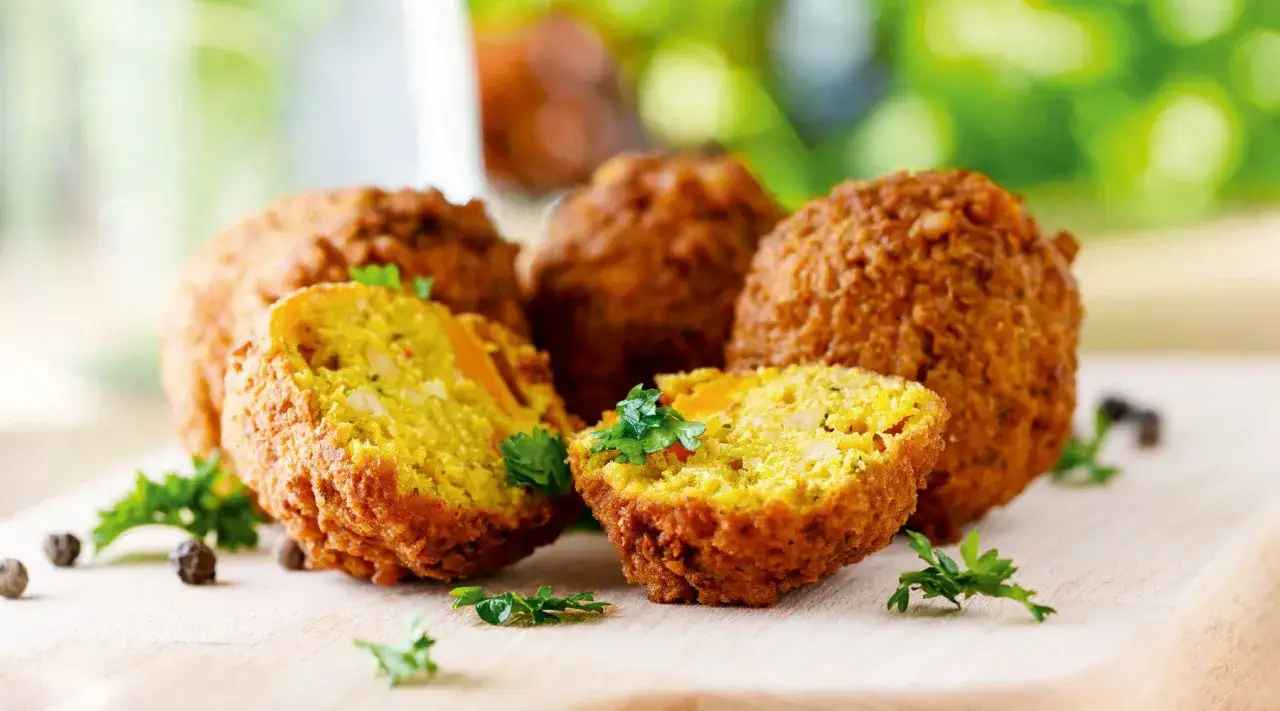 Goldbraune Falafel, eines von vielen leckeren falafel rezept Ideen, garniert mit Petersilie und Pfefferkörnern auf einem Holzbrett.