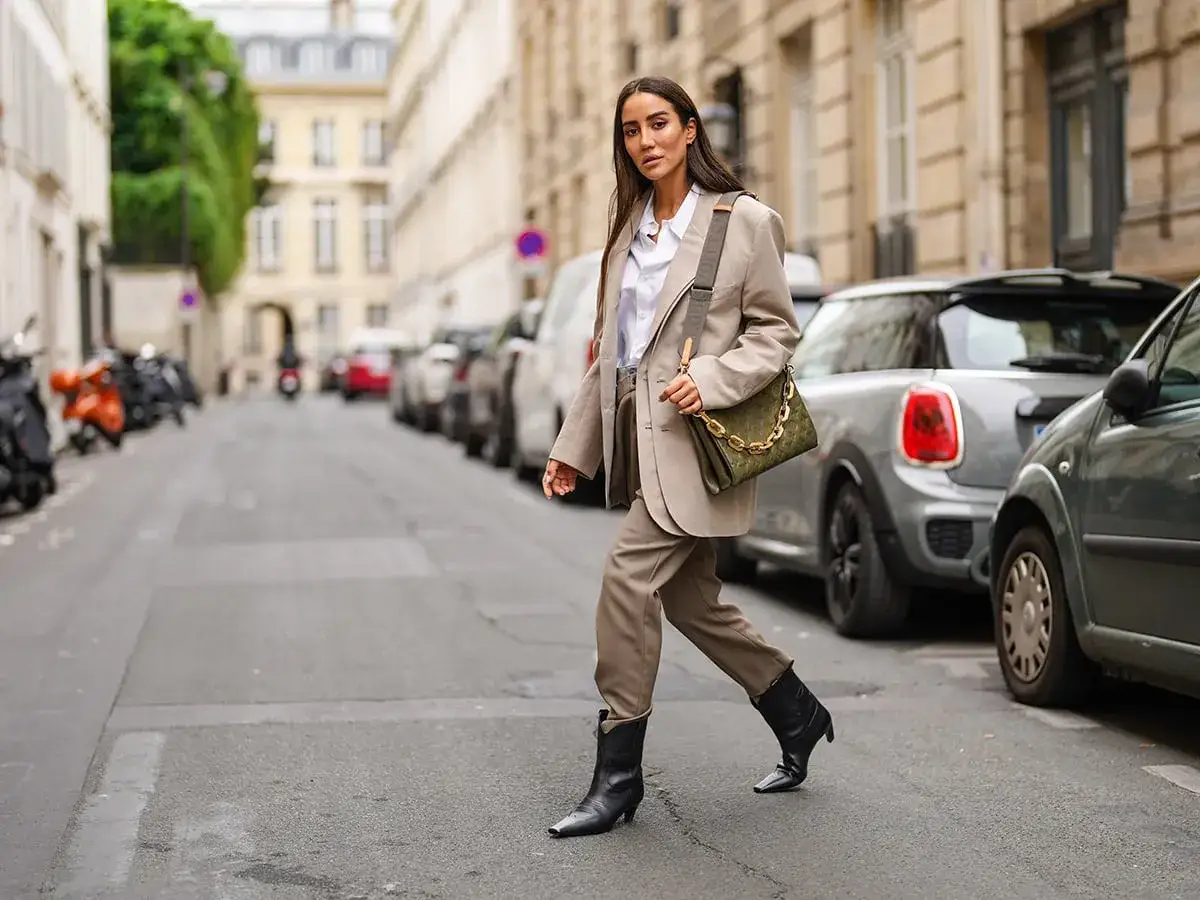 Donna con tailleur beige e stivali neri cammina per strada, un'ispirazione per i look autunnali.