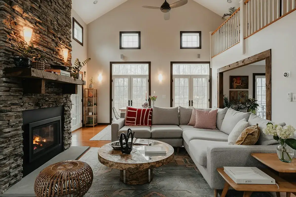 Acogedora sala de estar con chimenea de piedra, sof&aacute; seccional gris y mesa de centro r&uacute;stica, todo con un encantador estilo farmhouse.