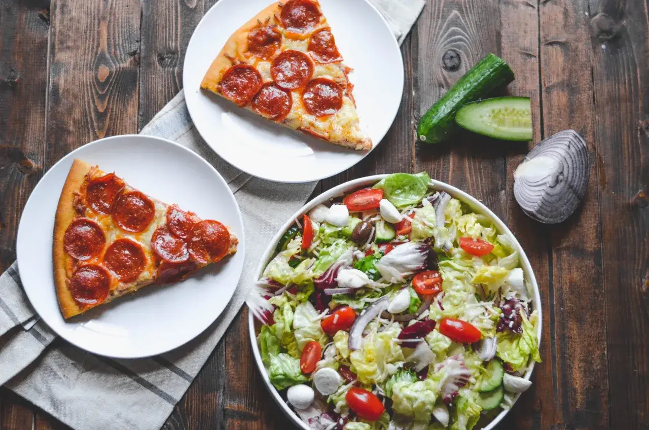 Två bitar pepperoni pizza och en typisk italiensk sallad med tomater, mozzarella och oliver.