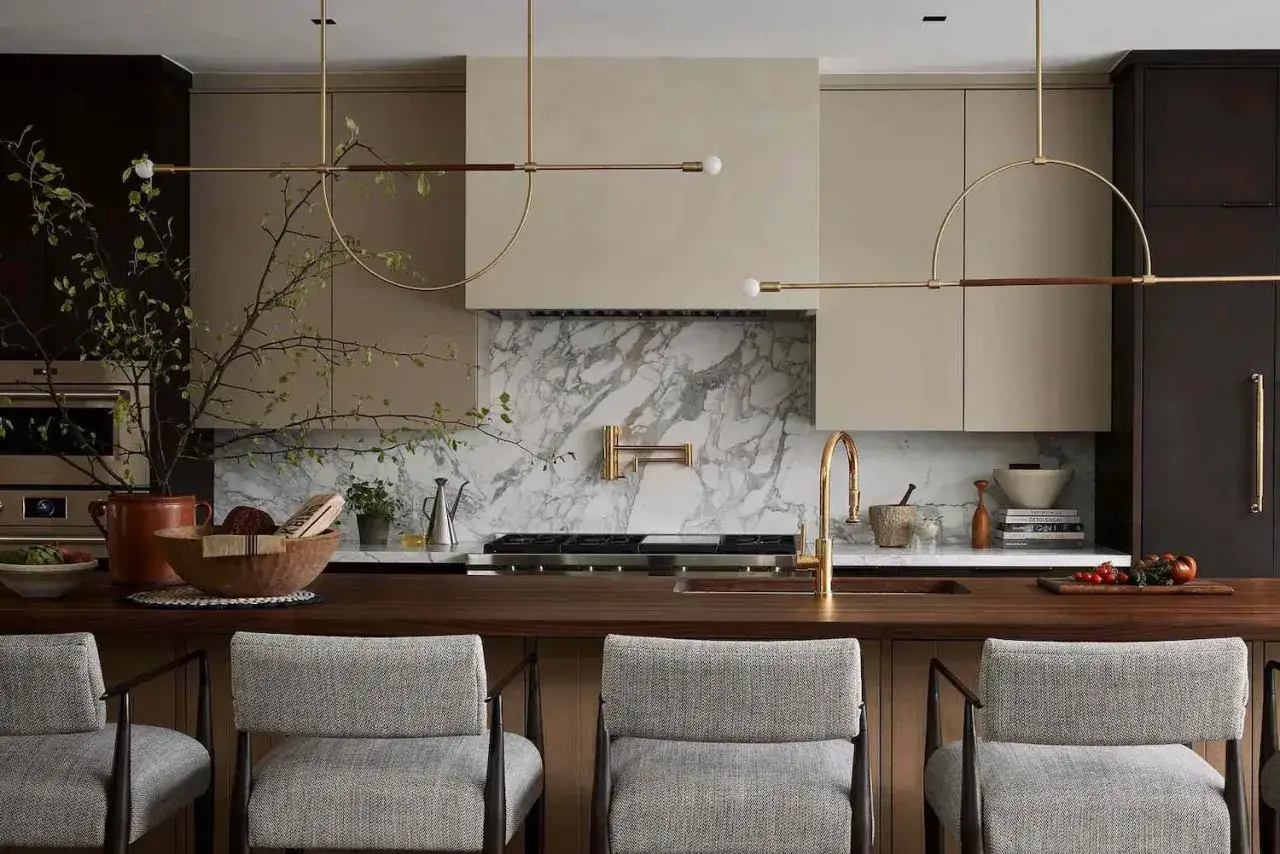 Beżowa kuchnia inspiracje: nowoczesne meble, marmurowy backsplash, złote baterie i stylowe lampy tworzą elegancką przestrzeń.
