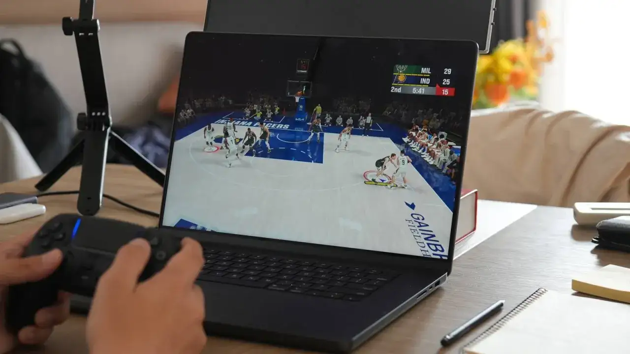Gracz steruje koszykarzami w grze na MacBooku, używając kontrolera.
