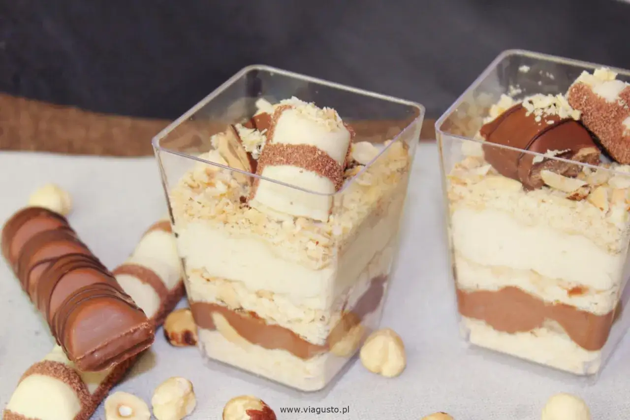 Pyszne ciasto kinder bueno z mascarpone w pucharkach, przełożone kremem i czekoladą, ozdobione orzechami i batonikami.
