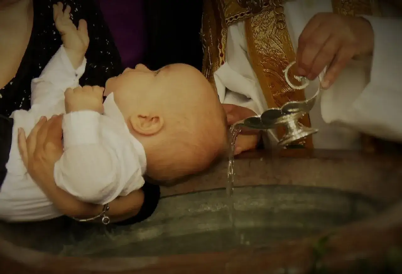 Chrzest dziecka, dylematy rodziców w rodzinach mieszanych. Woda święcona spływa na główkę niemowlęcia.