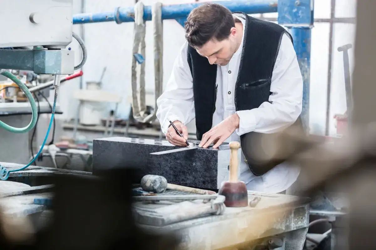 Kamieniarz precyzyjnie mierzy blok granitu. Zastanawiasz się, ile zarabia kamieniarz?