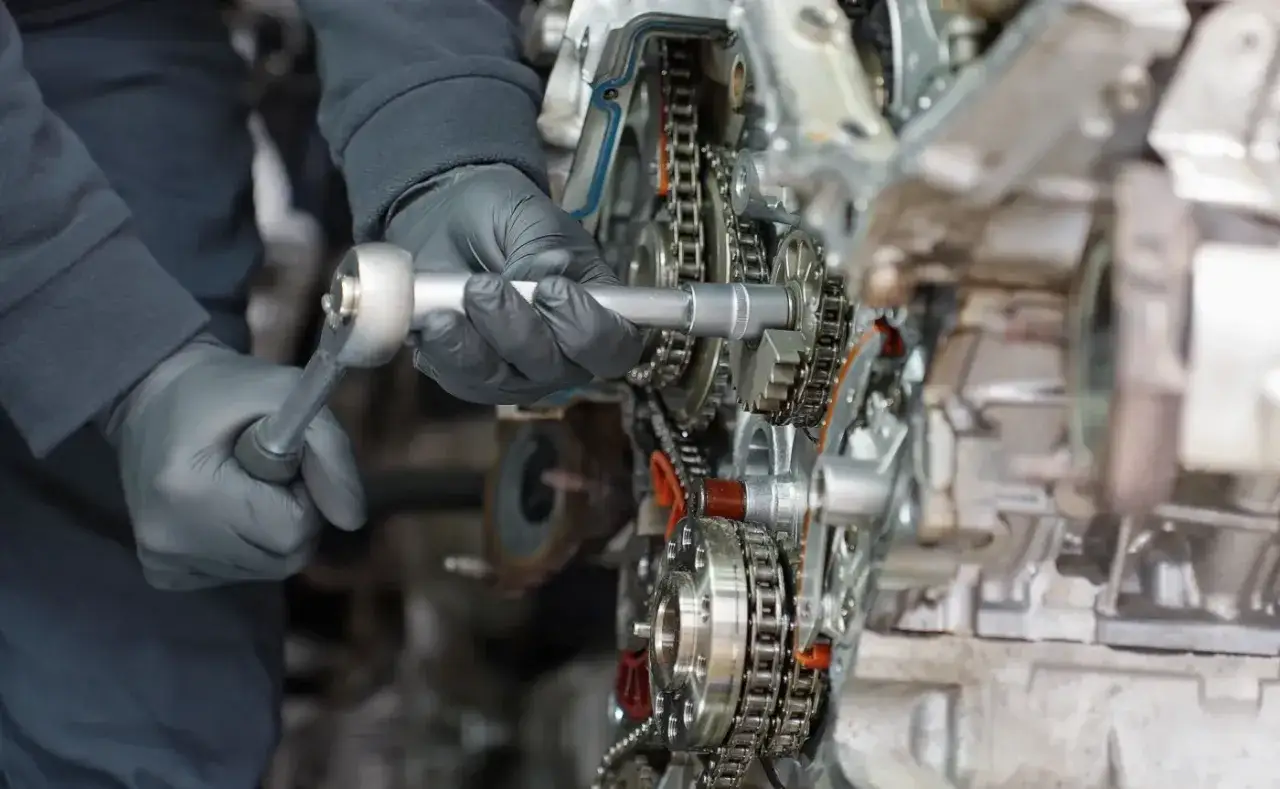Mechanik w czarnych rękawiczkach dokręca śrubę w silniku 1.6 PureTech. Widoczne są koła zębate i łańcuch rozrządu.