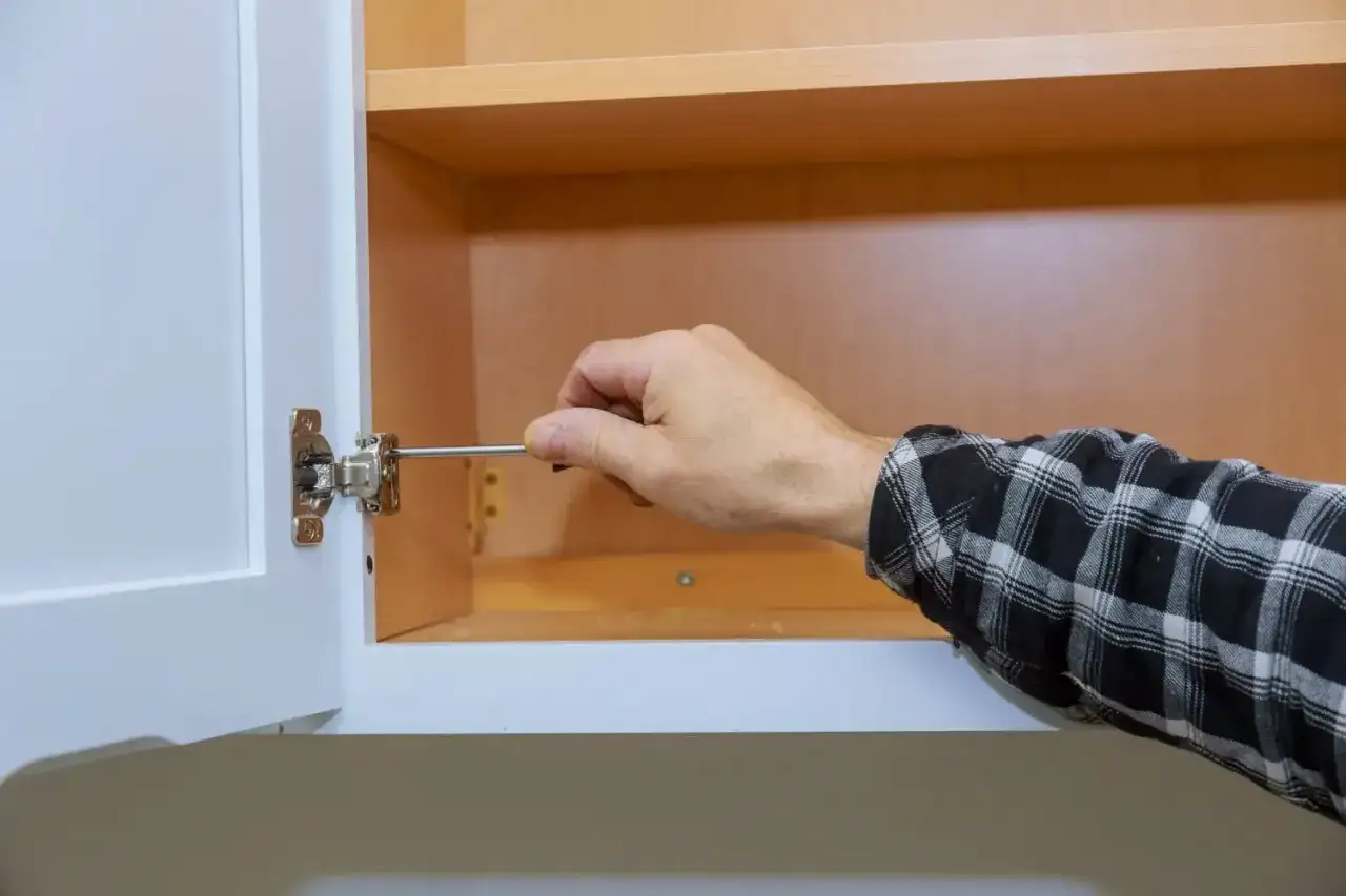 Mano ajustando puertas de armario con destornillador.