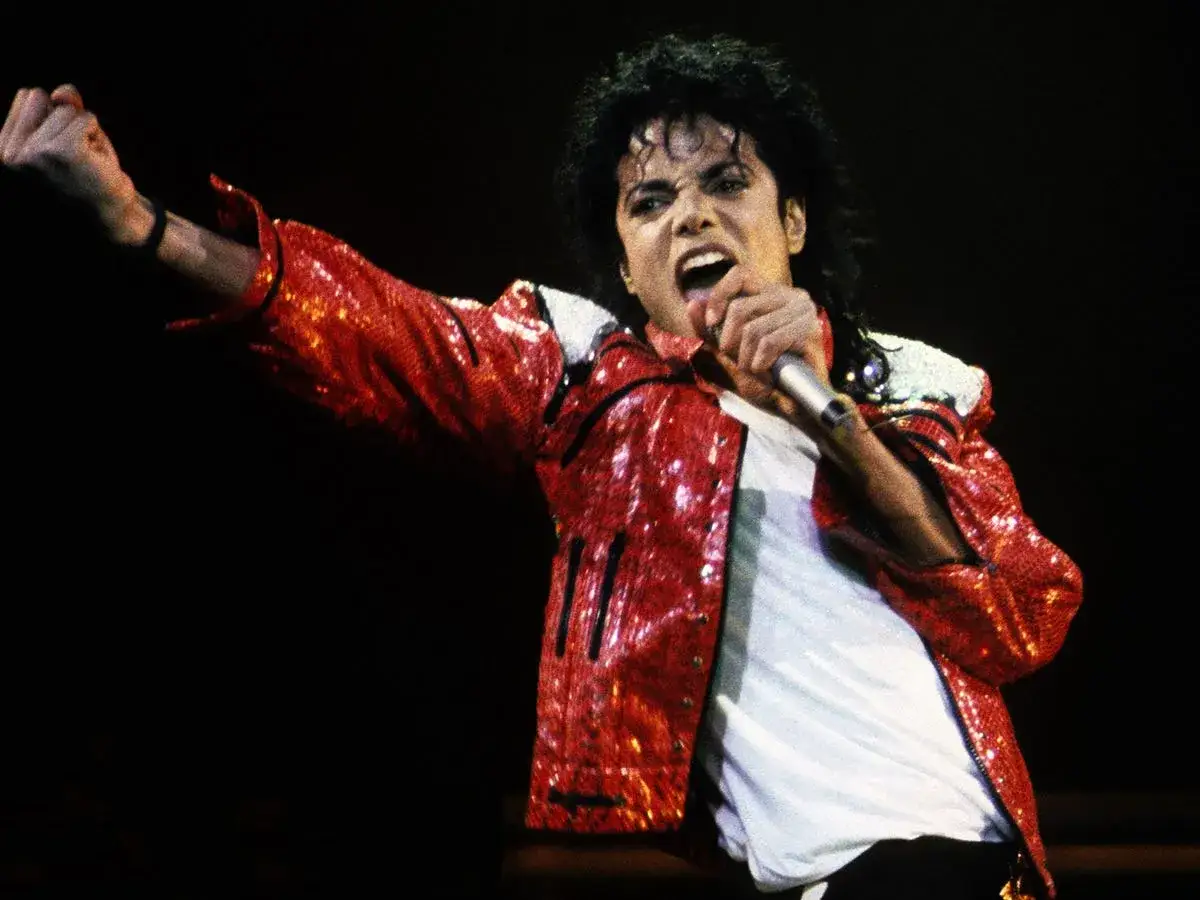 Michael Jackson w błyszczącej czerwonej kurtce śpiewa do mikrofonu. W którym roku zmarł Michael Jackson? 2009.