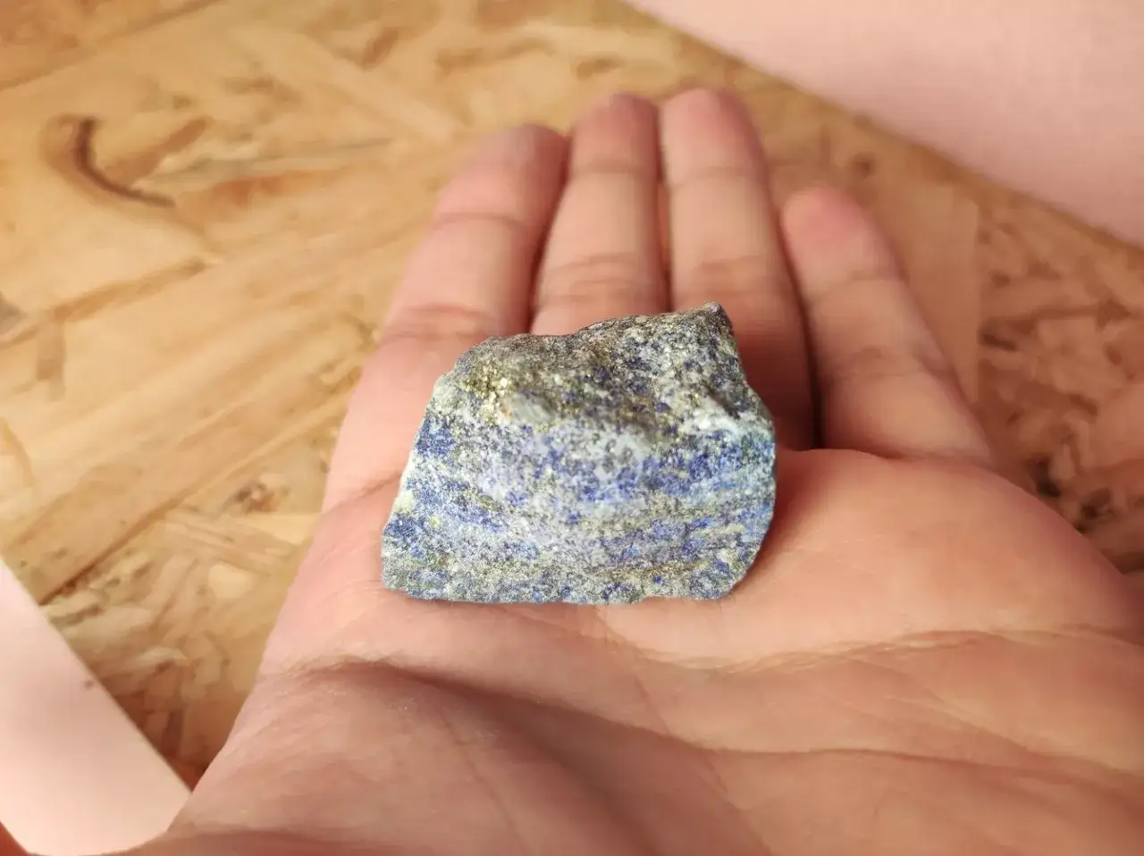 Pietra grezza di lapislazzuli con inclusioni dorate, tenuta in mano. Le sue vibranti proprietà blu sono visibili.