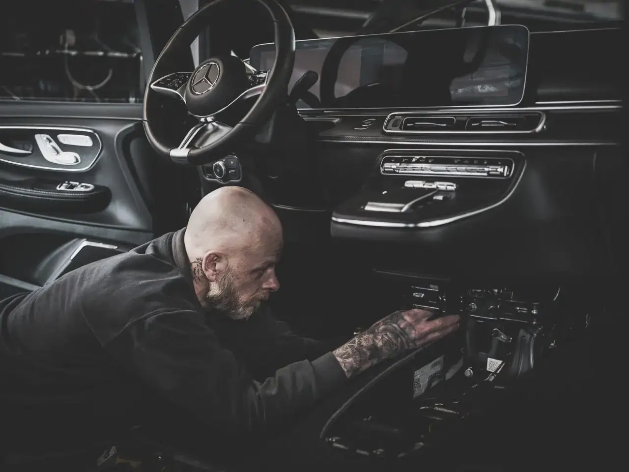 Mechaniker mit Tattoos arbeitet am Armaturenbrett. Der Anlasser dreht nicht, er sucht die Ursache im Fahrzeuginneren.