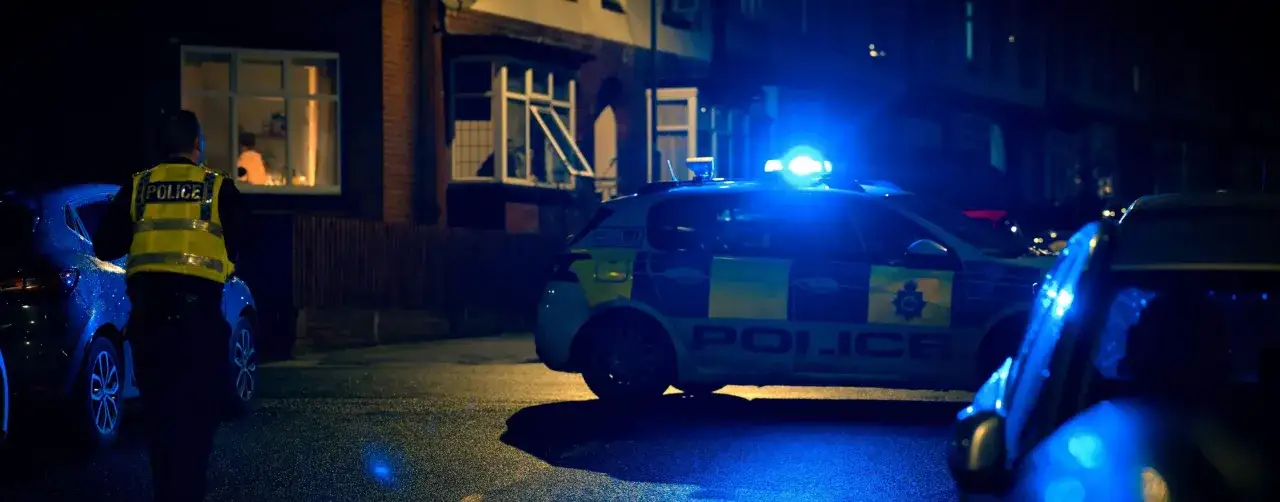 Nocna interwencja policji. Błyskające niebieskie światła policyjnego radiowozu i funkcjonariusz w kamizelce odblaskowej sugerują poważne konsekwencje zdarzenia.