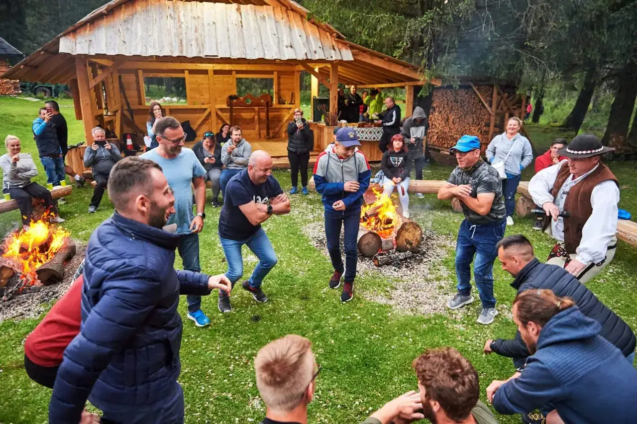 Grupa ludzi świętuje przy ognisku pod drewnianą wiatą. Idealne miejsce na wieczór kawalerski w góralskim stylu.