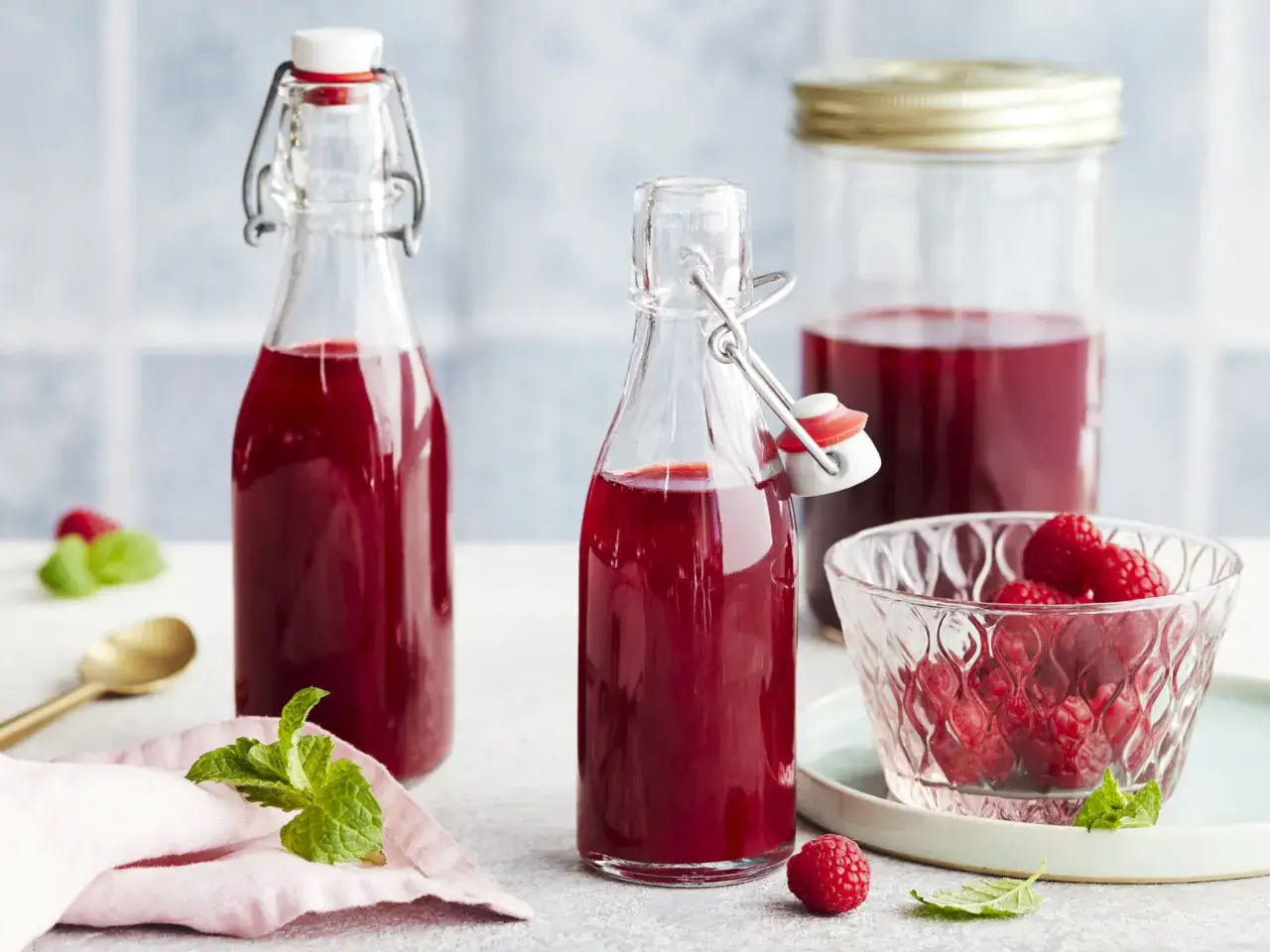 Himbeeressig selber machen: Flaschen mit rotem Essig, frische Himbeeren in einer Schale und Minze.