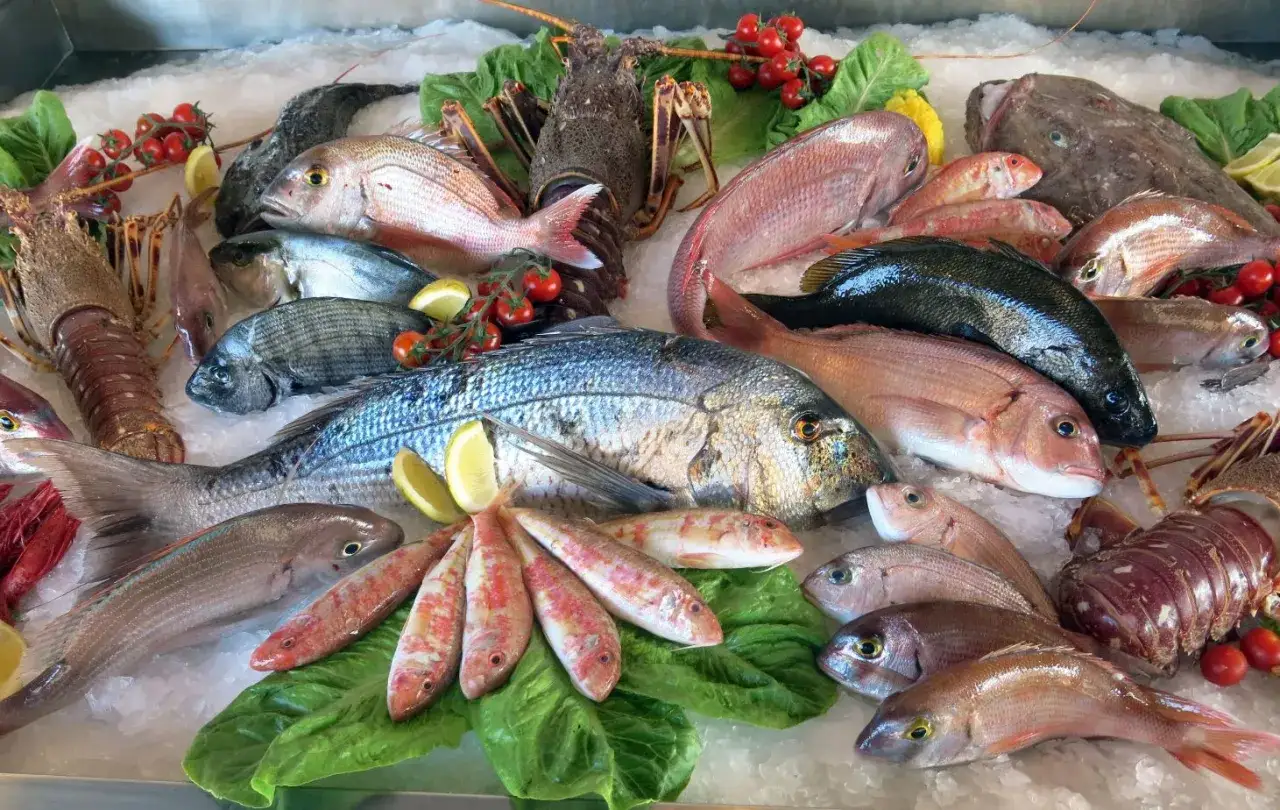 Un banco di pesce fresco su ghiaccio: aragoste, triglie, orate e un magnifico pesce azzurro, pronto per essere cucinato.