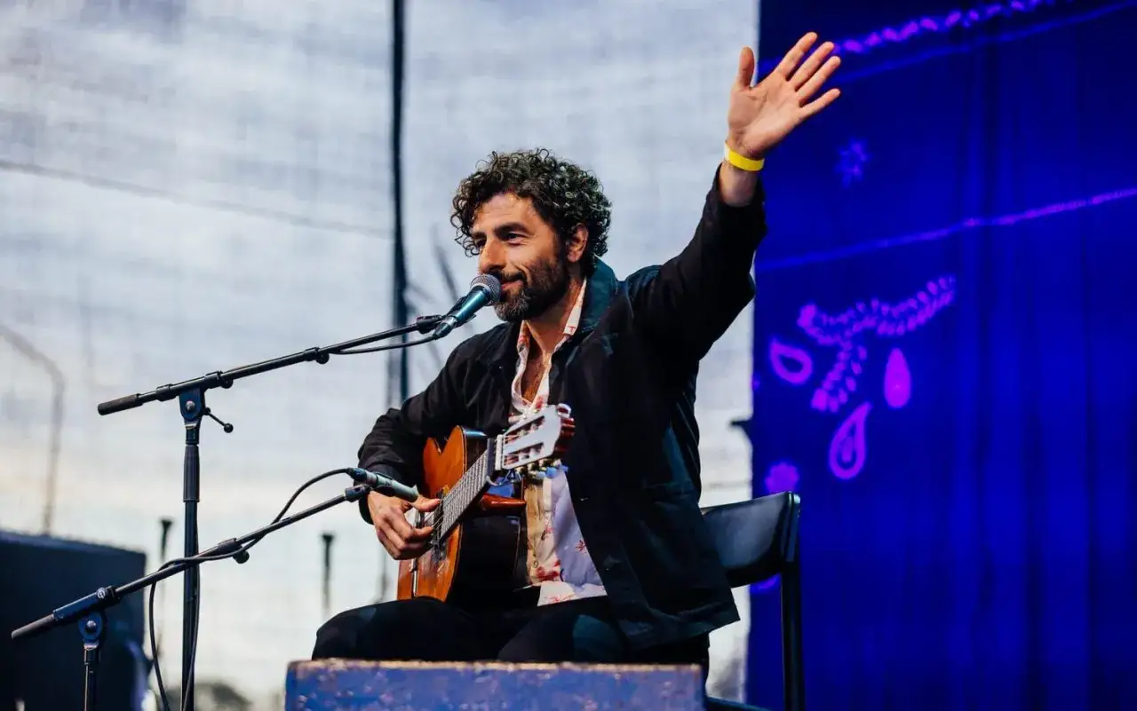 Lily Forsberg vinkar glatt medan hon spelar gitarr på scenen.