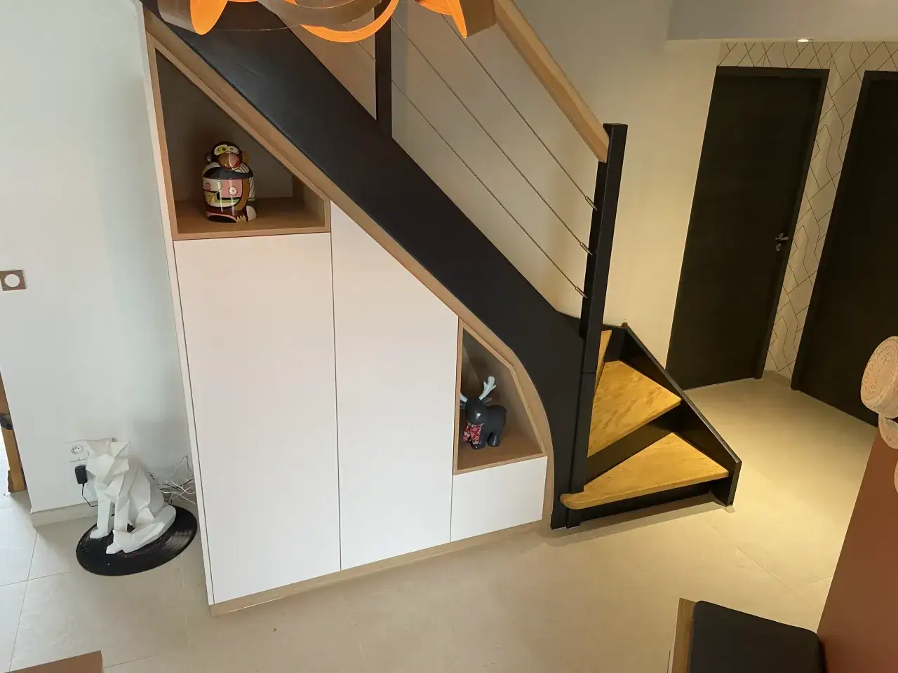 Am&eacute;nagement astucieux du rangement sous escalier avec des niches d&eacute;coratives et des portes blanches.