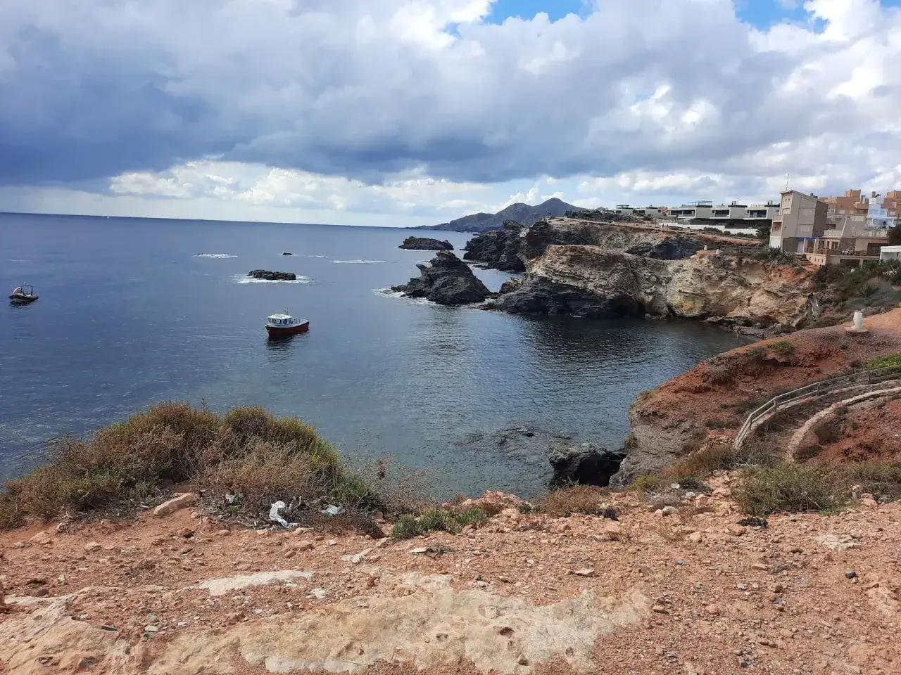 Felsige K&uuml;ste bei Cabo de Palos mit kleinen Booten im t&uuml;rkisfarbenen Meer und H&auml;usern am Hang.