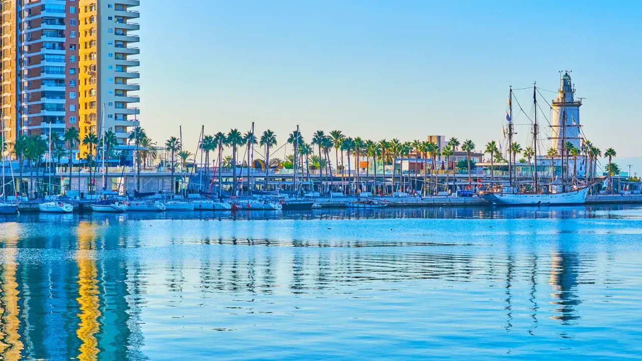 En vacker hamn med segelbåtar, ett högt modernt hus och en fyr. En perfekt vy att se i Malaga.