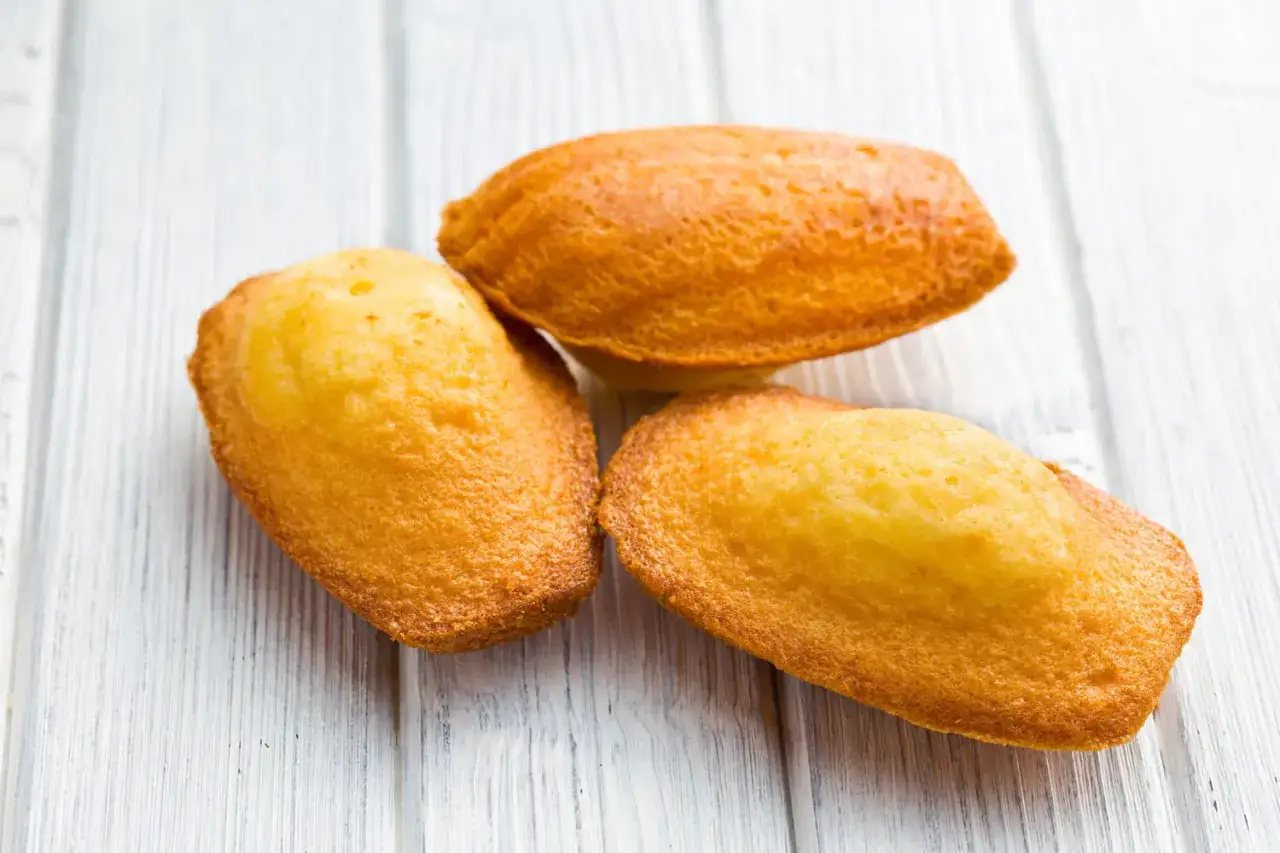 Trois biscuits madeleine dor&eacute;s, faits maison avec le Thermomix, sur un fond de bois clair.