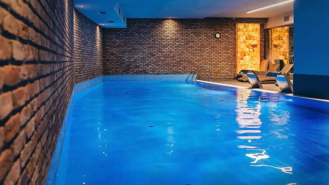 Basen w hotelu Almond, z ceglanymi ścianami i relaksującymi leżakami.