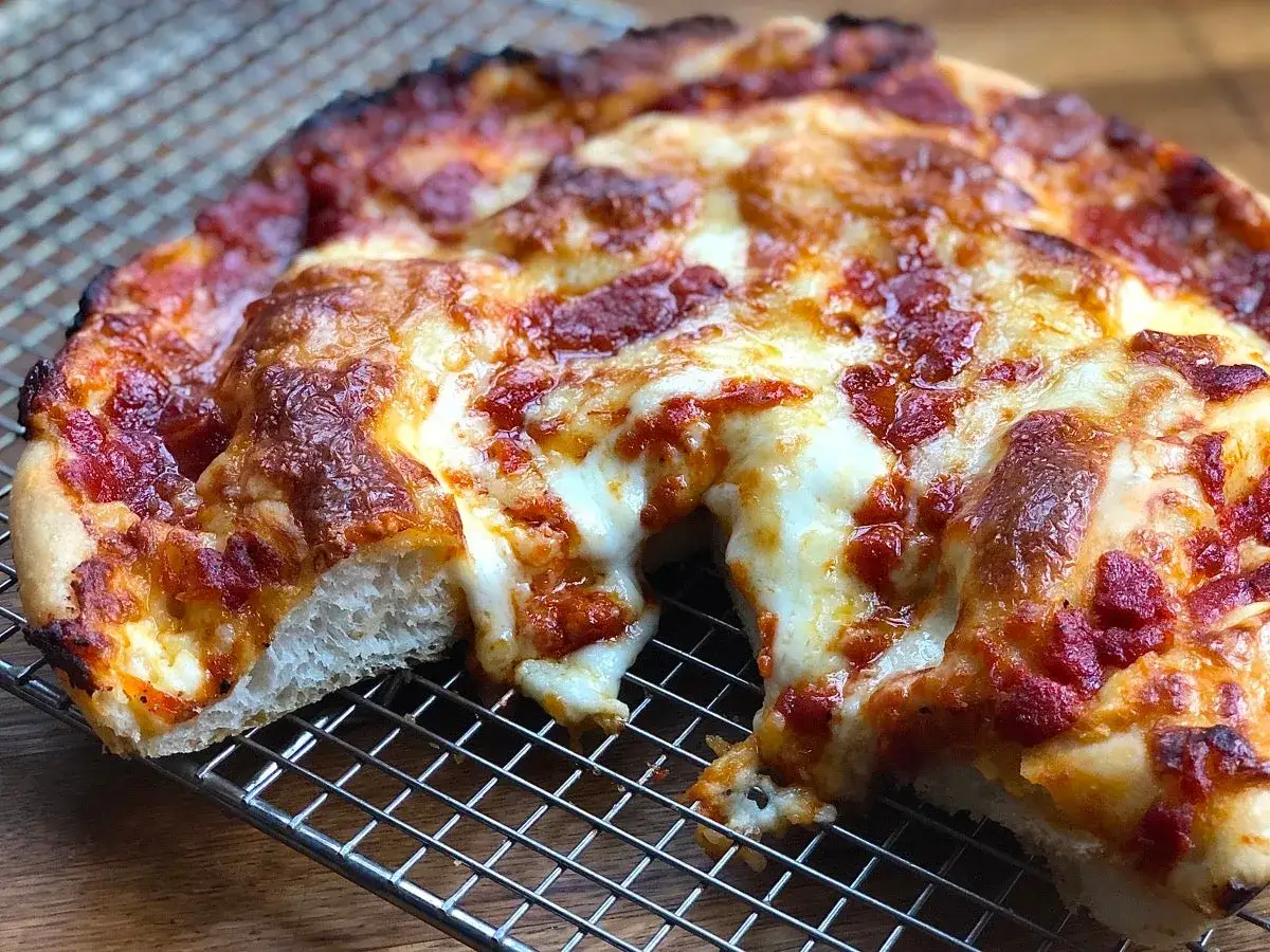 Gorąca pizza z ciągnącym się serem do pizzy, na metalowej kratce.
