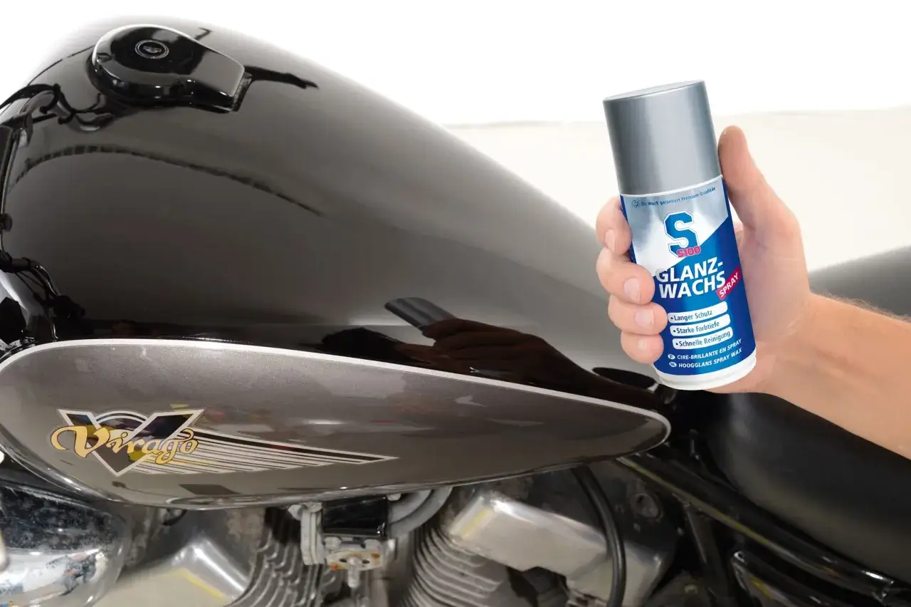 Mano che tiene uno spray per la lucidatura plastica di una moto.