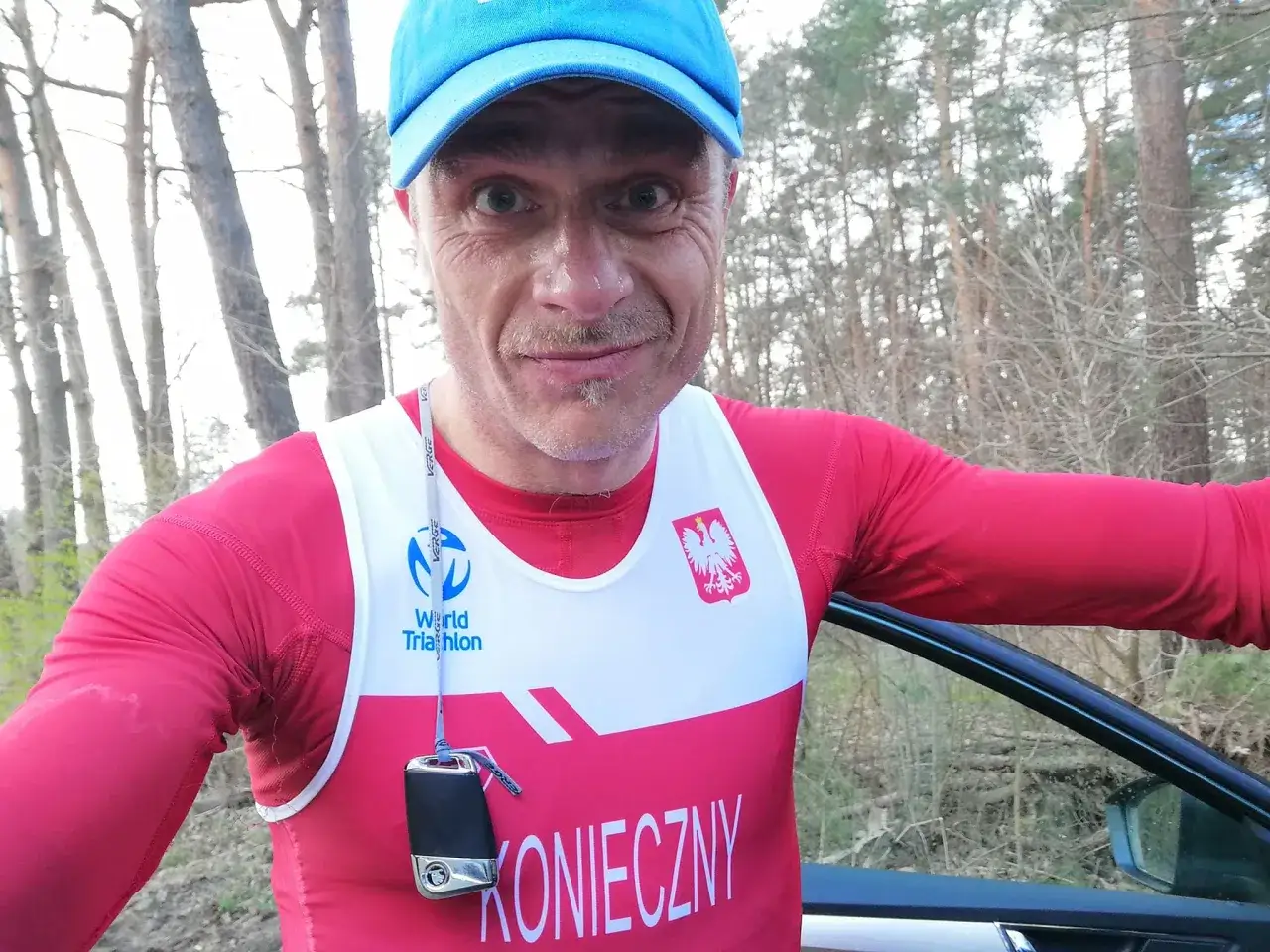 Marcin Konieczny w stroju triathlonowym z orłem na piersi, zmęczony po treningu w lesie.