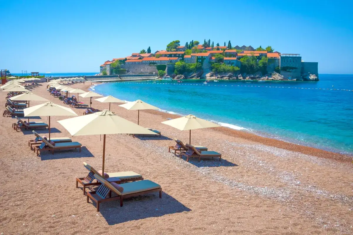 Sveti Stefan, Czarnogóra. Piękna plaża z leżakami i parasolami. Ceny wakacji w Czarnogórze mogą być różne, ale widok jest bezcenny.