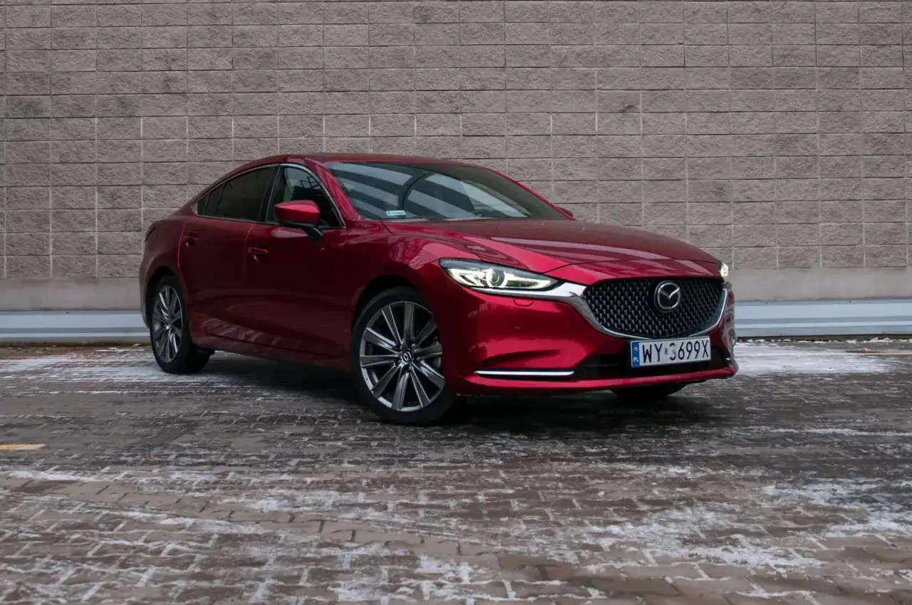 Czerwona Mazda 6 2.0 benzyna zaparkowana na ośnieżonym bruku przed ceglanym murem.