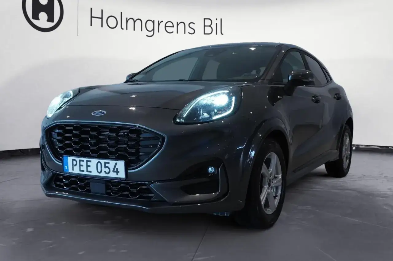 M&ouml;rkgr&aring; Ford Puma Hybrid med lysande str&aring;lkastare och registreringsskylten PEE 054.