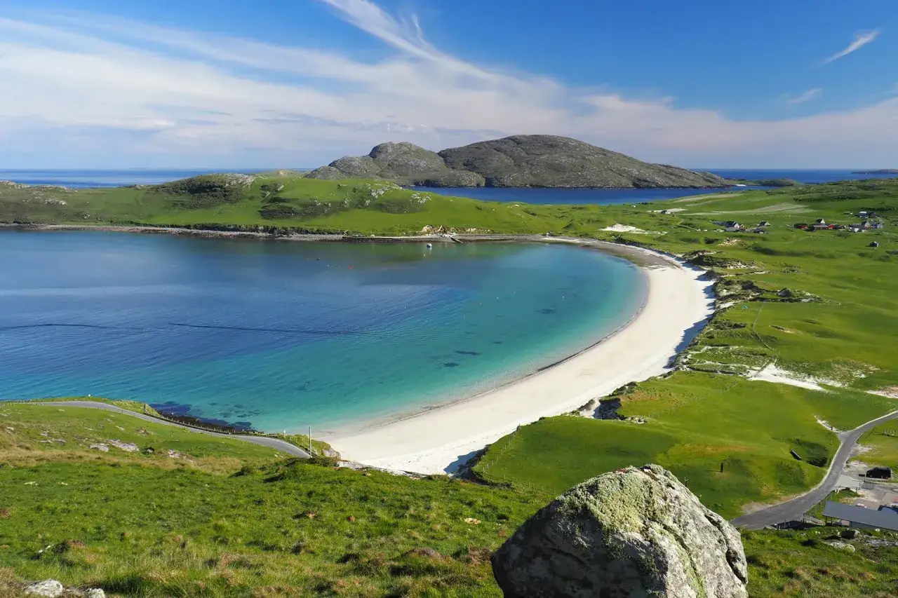 En grönskande, böljande landskap på Yttre Hebriderna med en turkos vik och en vit sandstrand.