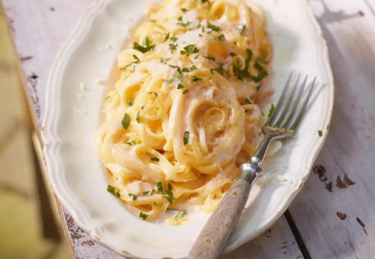 Cremige Pasta mit zitronensauce, garniert mit Petersilie und Parmesan. Ein Gabel liegt daneben.
