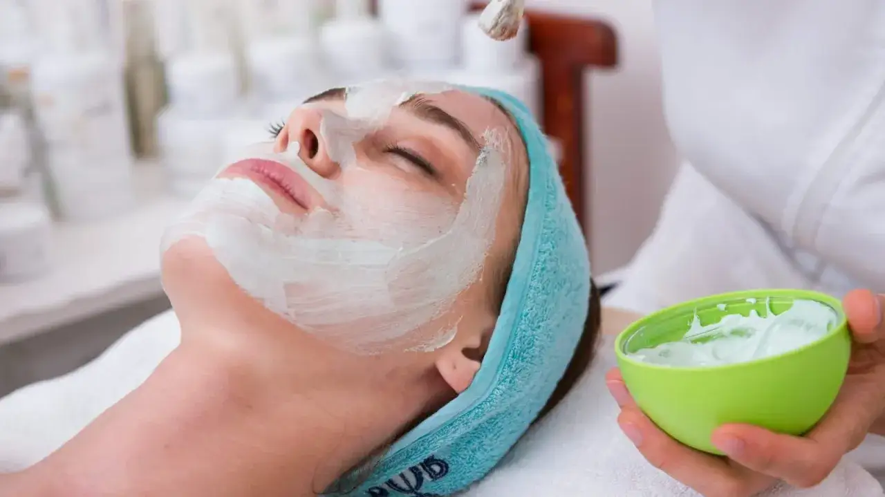 Une femme re&ccedil;oit un masque aloe vera visage. Une main tient un bol vert rempli de cr&egrave;me, tandis qu'un pinceau applique le masque sur son visage.